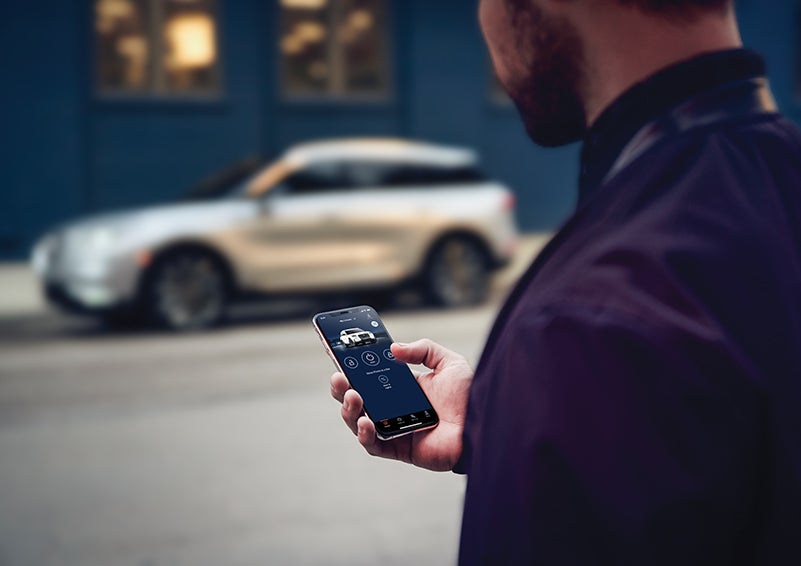A person is shown interacting with a smartphone to connect to a Lincoln vehicle across the street. | Johnson Sewell Lincoln in Marble Falls TX